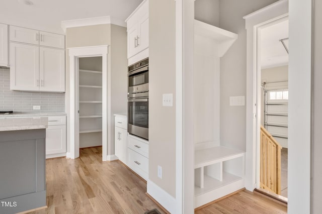 kitchen with light wood-type flooring, white cabinets, stainless steel double oven, light stone countertops, and backsplash