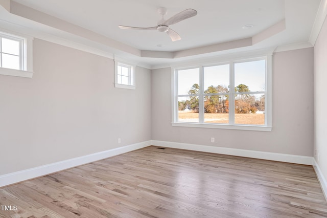 empty room with a raised ceiling, ceiling fan, and light hardwood / wood-style flooring