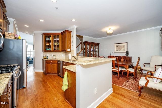 kitchen with stainless steel appliances, brown cabinetry, a sink, light stone countertops, and a peninsula