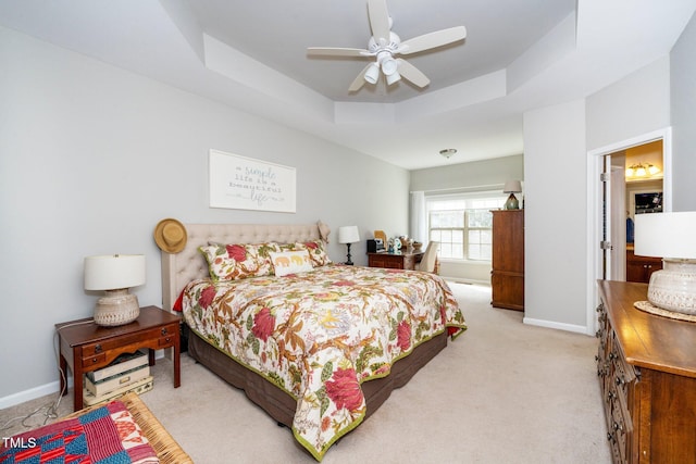 bedroom featuring a raised ceiling, light colored carpet, ceiling fan, and baseboards