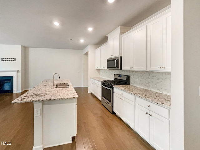 kitchen with sink, stainless steel appliances, light stone countertops, an island with sink, and white cabinets