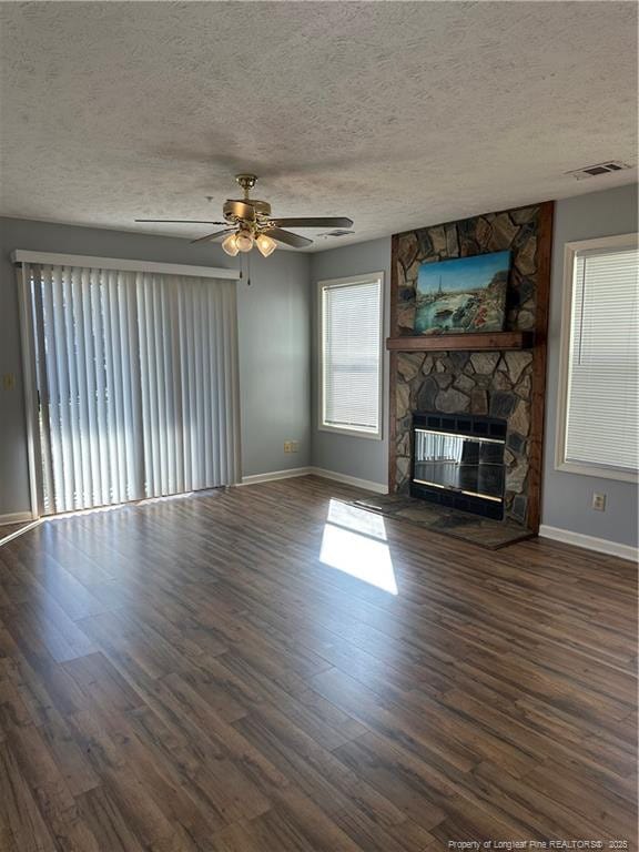 unfurnished living room with ceiling fan, a stone fireplace, dark wood-type flooring, and a textured ceiling