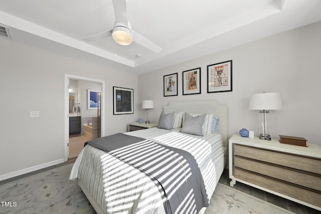 bedroom with a raised ceiling, ceiling fan, connected bathroom, and light hardwood / wood-style floors