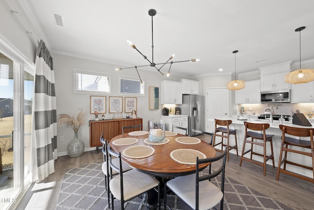 dining space featuring ornamental molding, dark wood-type flooring, sink, and a notable chandelier