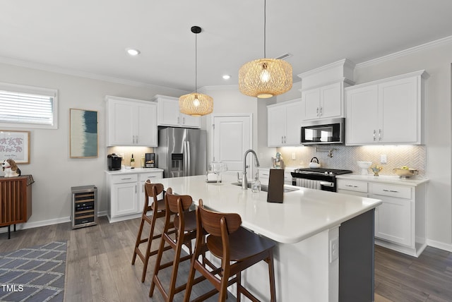 kitchen with pendant lighting, sink, appliances with stainless steel finishes, white cabinetry, and a center island with sink