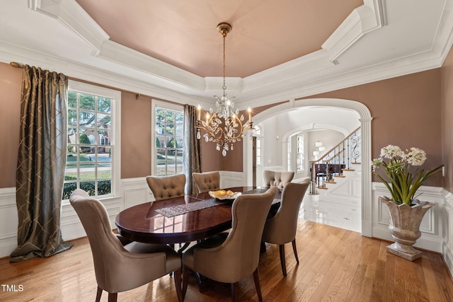 dining space with crown molding, a tray ceiling, light hardwood / wood-style floors, and a chandelier