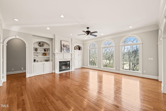 unfurnished living room with crown molding, built in features, light hardwood / wood-style floors, and ceiling fan