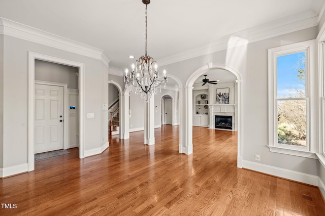 unfurnished dining area featuring ornamental molding, ceiling fan with notable chandelier, hardwood / wood-style floors, and built in shelves