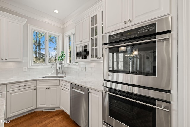 kitchen with stainless steel appliances, white cabinetry, light stone countertops, and sink