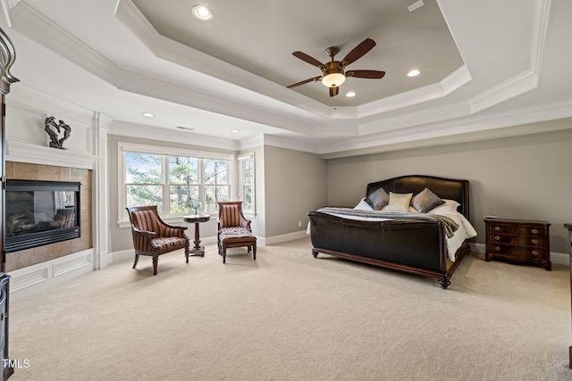 carpeted bedroom featuring a tiled fireplace, a tray ceiling, crown molding, and ceiling fan