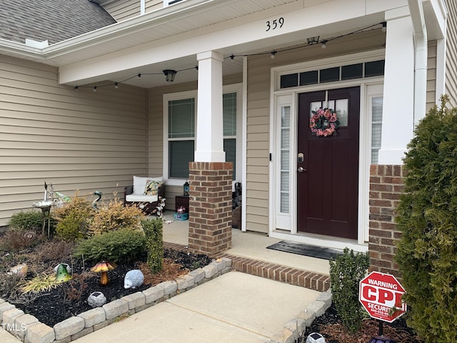 view of exterior entry featuring a shingled roof, a porch, and brick siding