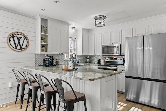 kitchen featuring a breakfast bar, white cabinetry, kitchen peninsula, stainless steel appliances, and light stone countertops