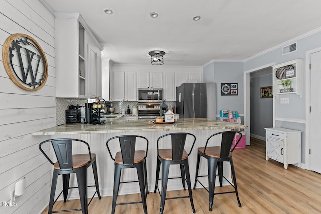 kitchen with light hardwood / wood-style flooring, appliances with stainless steel finishes, kitchen peninsula, decorative backsplash, and white cabinets