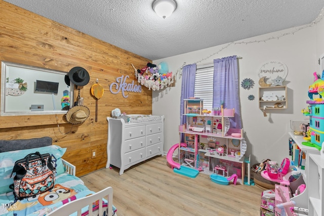 bedroom featuring wood walls, a textured ceiling, and light hardwood / wood-style flooring