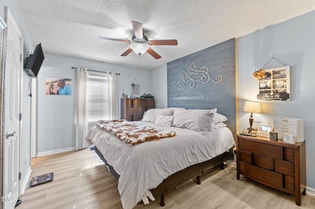 bedroom featuring a ceiling fan, light wood-style floors, baseboards, and a textured ceiling