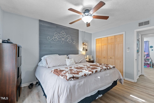 bedroom featuring a closet, wood walls, a textured ceiling, and light hardwood / wood-style flooring