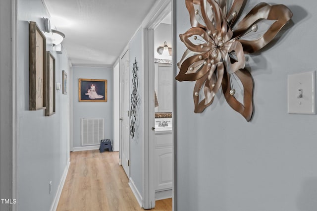 hallway with a sink, visible vents, baseboards, and light wood finished floors