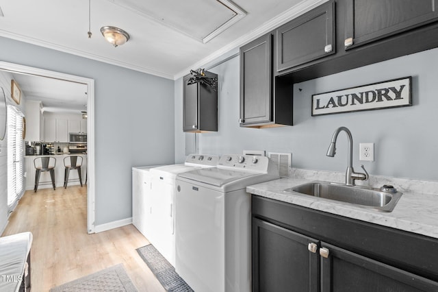 laundry room featuring a sink, washing machine and dryer, cabinet space, crown molding, and light wood finished floors