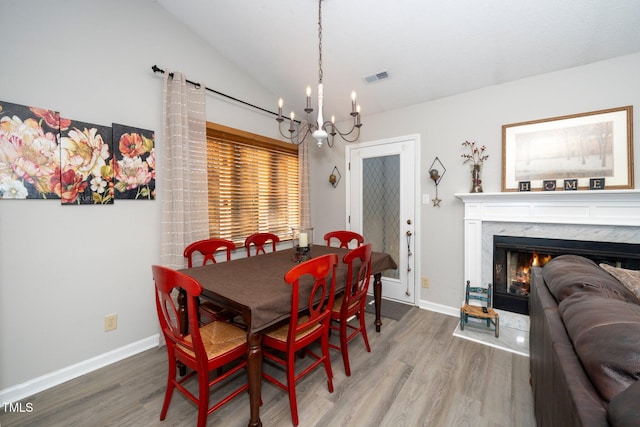 dining area featuring lofted ceiling, a chandelier, a high end fireplace, and wood-type flooring