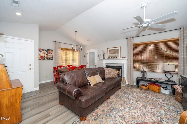 living room featuring vaulted ceiling, ceiling fan with notable chandelier, a fireplace, and light hardwood / wood-style floors