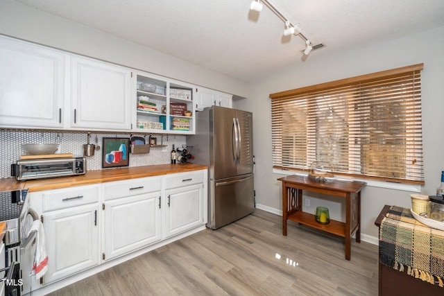 kitchen with wood counters, stainless steel refrigerator, light hardwood / wood-style floors, decorative backsplash, and white cabinets