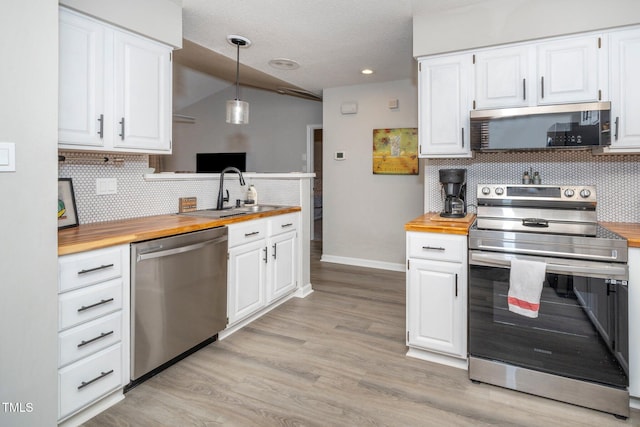 kitchen featuring appliances with stainless steel finishes, butcher block counters, hanging light fixtures, white cabinetry, and light hardwood / wood-style floors