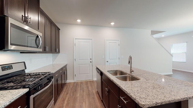 kitchen featuring sink, light stone counters, appliances with stainless steel finishes, an island with sink, and backsplash