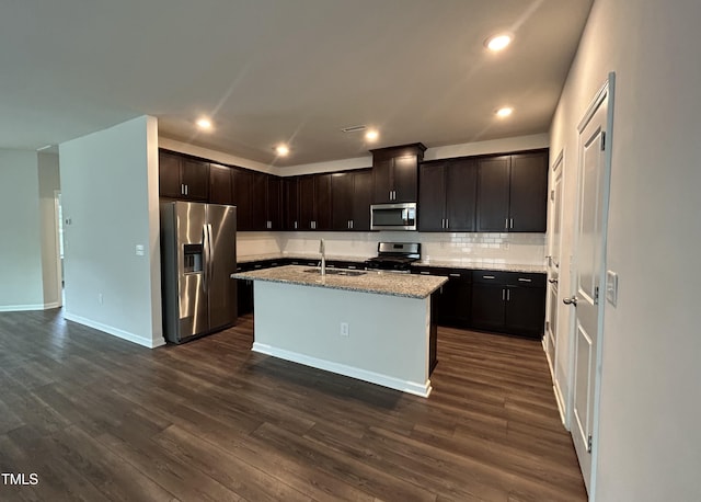 kitchen featuring appliances with stainless steel finishes, dark hardwood / wood-style floors, sink, a kitchen island with sink, and light stone countertops