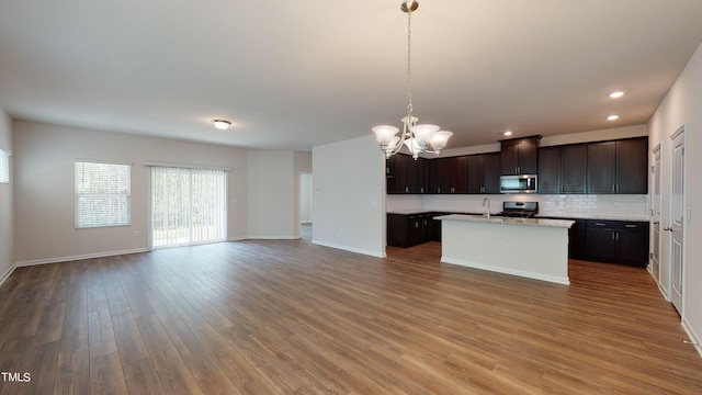 kitchen featuring decorative light fixtures, dark brown cabinets, a center island with sink, dark hardwood / wood-style floors, and backsplash