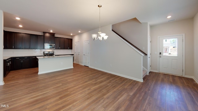 kitchen featuring dark brown cabinets, appliances with stainless steel finishes, dark hardwood / wood-style floors, pendant lighting, and a kitchen island with sink