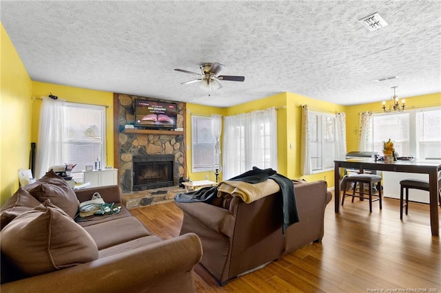 living room featuring hardwood / wood-style flooring, a stone fireplace, ceiling fan with notable chandelier, and a textured ceiling