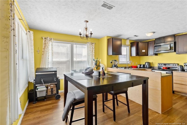 kitchen with sink, light hardwood / wood-style flooring, an inviting chandelier, stainless steel appliances, and decorative light fixtures