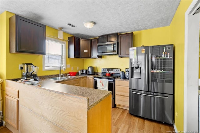 kitchen with sink, a textured ceiling, kitchen peninsula, stainless steel appliances, and light hardwood / wood-style floors