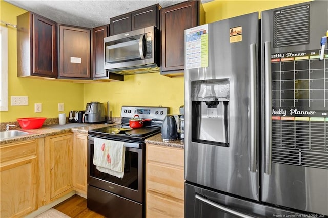 kitchen with stainless steel appliances, light stone countertops, hardwood / wood-style flooring, and a textured ceiling