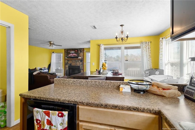 kitchen featuring a stone fireplace, decorative light fixtures, a textured ceiling, beverage cooler, and ceiling fan with notable chandelier