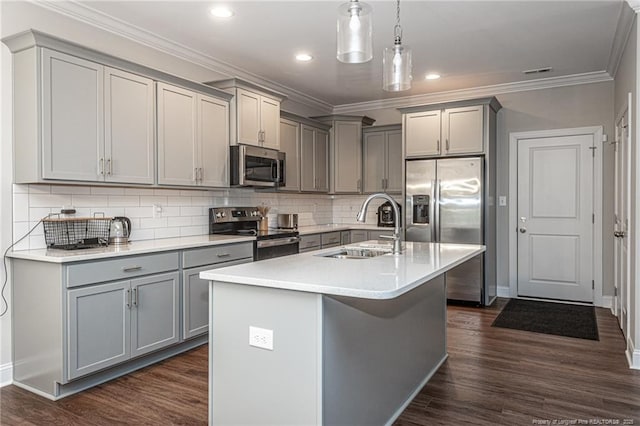 kitchen with appliances with stainless steel finishes, dark hardwood / wood-style floors, decorative light fixtures, an island with sink, and sink