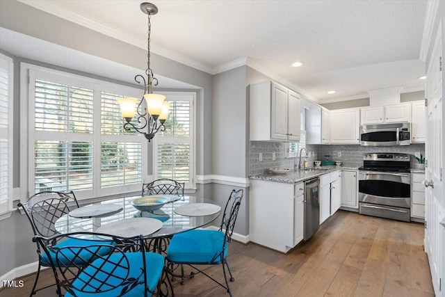 kitchen with pendant lighting, sink, appliances with stainless steel finishes, white cabinetry, and wood-type flooring