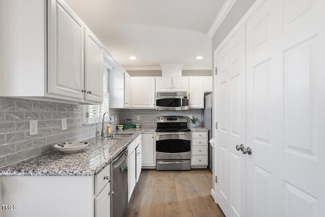 kitchen with white cabinetry, sink, stainless steel appliances, crown molding, and light stone countertops