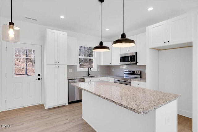 kitchen featuring appliances with stainless steel finishes, white cabinetry, sink, hanging light fixtures, and a center island