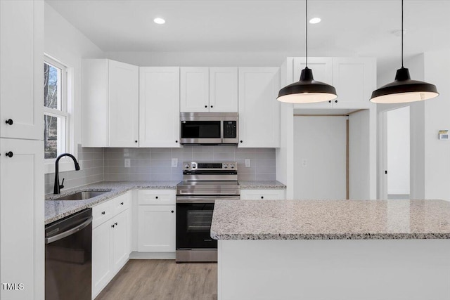 kitchen with sink, white cabinetry, hanging light fixtures, stainless steel appliances, and light stone countertops