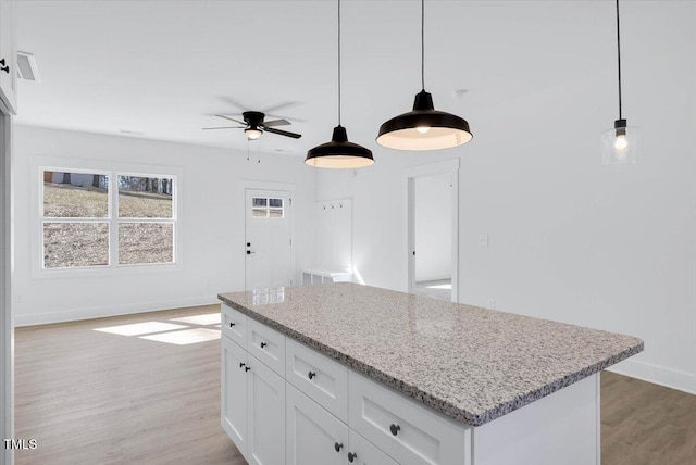 kitchen featuring a kitchen island, pendant lighting, light stone countertops, light hardwood / wood-style floors, and white cabinets