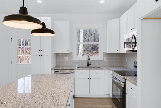 kitchen featuring stainless steel appliances, sink, white cabinets, and decorative light fixtures