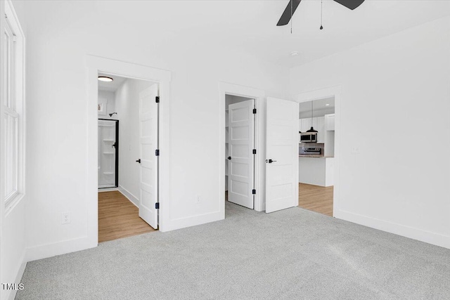 unfurnished bedroom featuring a walk in closet, light colored carpet, connected bathroom, and ceiling fan