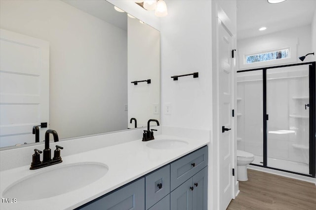 bathroom featuring wood-type flooring, toilet, a shower with shower door, and vanity