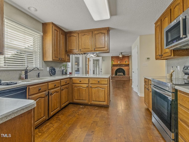 kitchen featuring a fireplace, sink, dark hardwood / wood-style flooring, kitchen peninsula, and stainless steel appliances