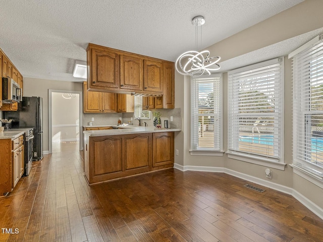 kitchen with dark wood-type flooring, an inviting chandelier, stainless steel appliances, decorative light fixtures, and kitchen peninsula