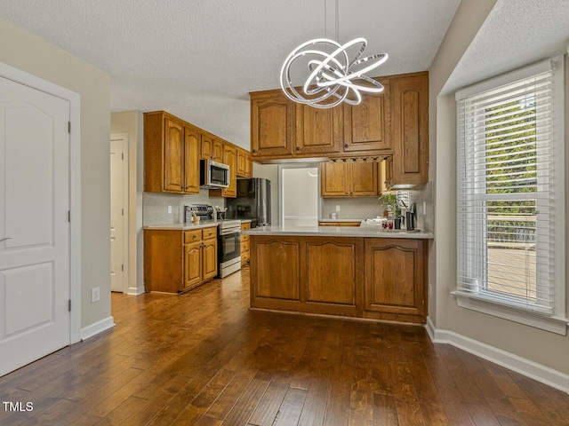 kitchen with appliances with stainless steel finishes, pendant lighting, dark hardwood / wood-style flooring, decorative backsplash, and kitchen peninsula