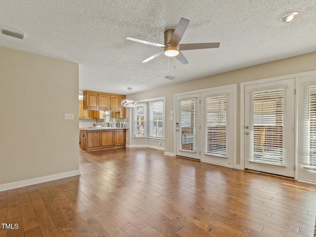 unfurnished living room with ceiling fan, a textured ceiling, and light wood-type flooring