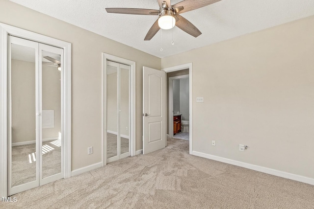 unfurnished bedroom featuring ceiling fan, two closets, light colored carpet, and a textured ceiling