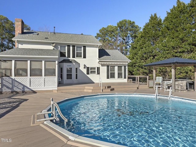 view of pool featuring a wooden deck, a gazebo, and a sunroom